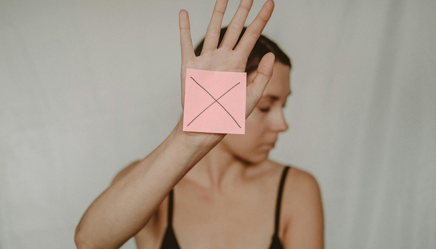 Woman holding up her hand with a pink sticky note marked with an X, signaling stop or setting a boundary