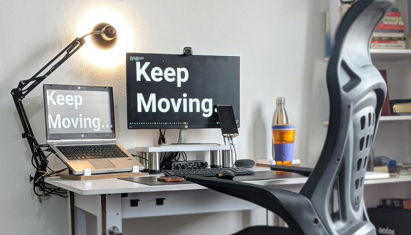 Minimal home office setup with a desk, laptop and monitor displaying “Keep Moving,” ergonomic chair, desk lamp, and organized workspace.