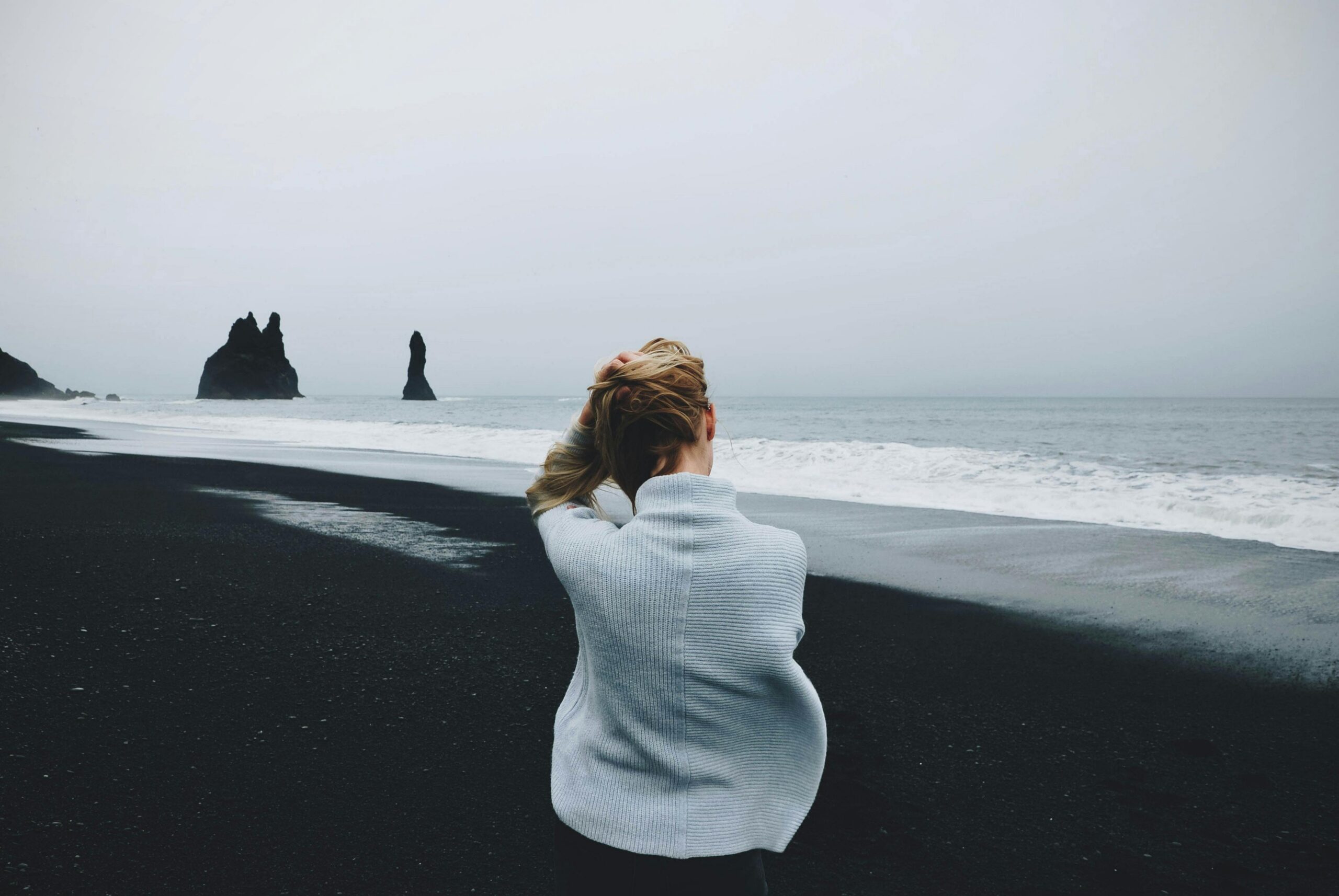 Woman standing on a black sand beach looking toward the ocean, reflecting on what comes next